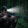 Nightforge Stirnlampe, Jäger zielt mit Gewehr und Zielfernrohr, Stirnlampe leuchtet den Wald aus