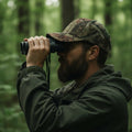 Jäger mit Camo Jagd-Cap beim Glasen mit Fernglas im Wald