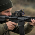 Prismenvisier mit Rotpunkt auf einem Gewehr im Anschlag, beide Augen offen