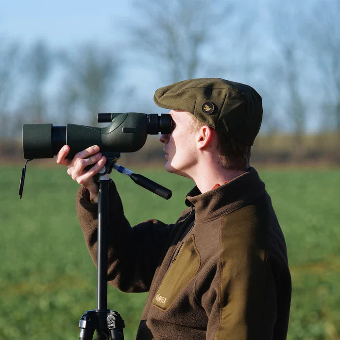 ZoomMeister Spektiv auf Stativ, Jäger in Grün blickt im Feld hindurch, Bäume im Hintergrund
