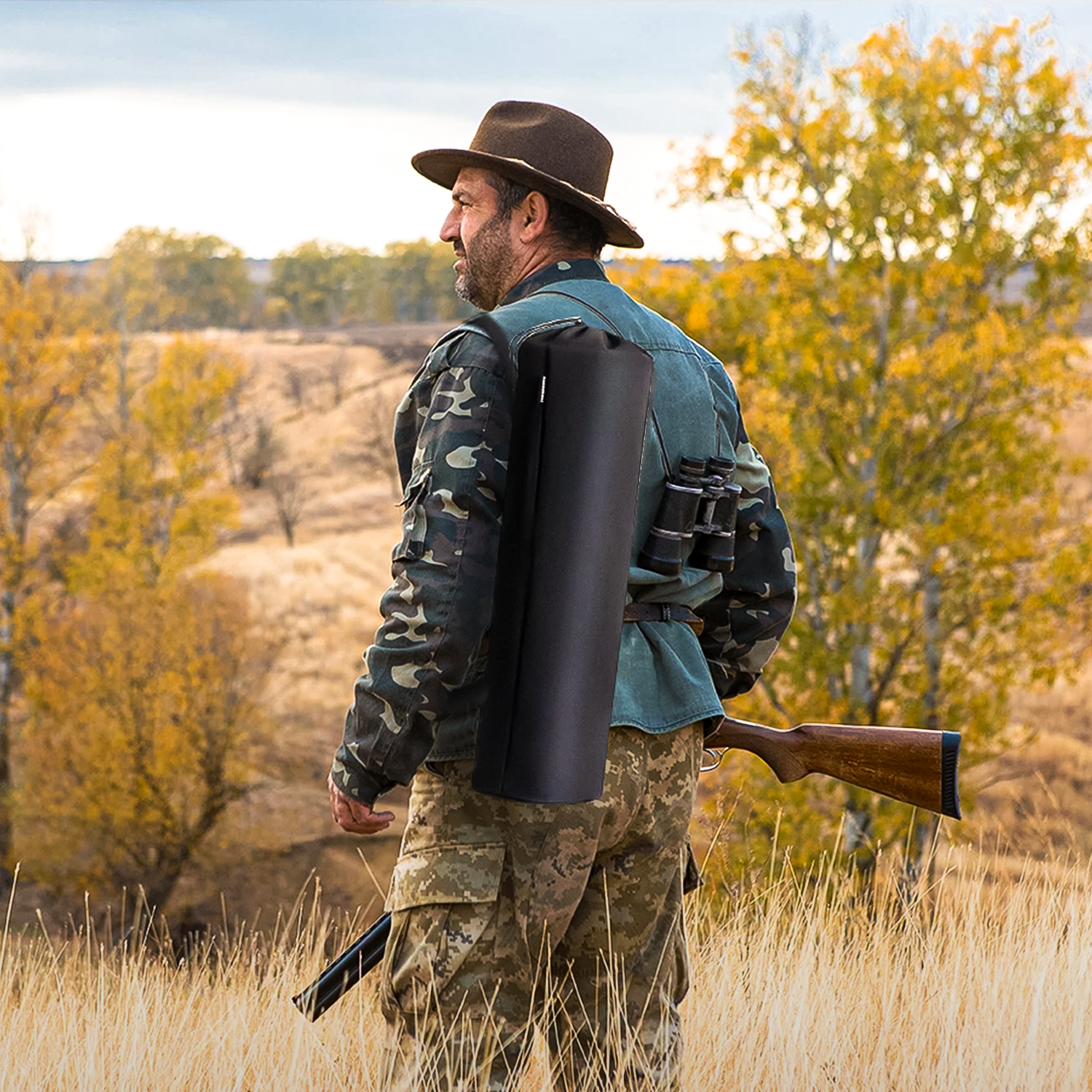 Jagdblind als Rucksackrolle gepackt, Jäger mit Gewehr und Fernglas im herbstlichen Feld